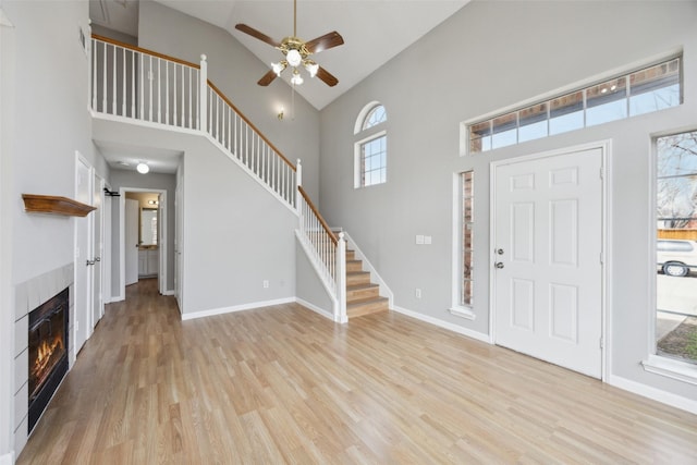 entrance foyer with baseboards, a tiled fireplace, stairs, light wood-style flooring, and a towering ceiling