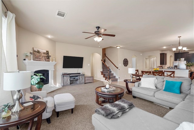 living room with visible vents, arched walkways, stairs, carpet flooring, and ceiling fan with notable chandelier