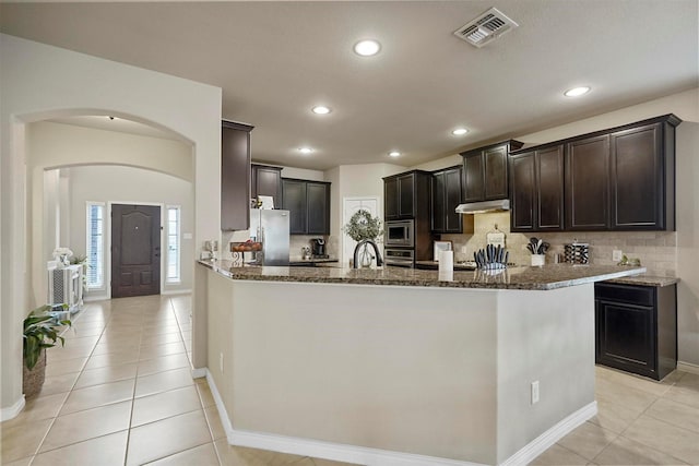 kitchen with under cabinet range hood, visible vents, dark stone countertops, and stainless steel appliances