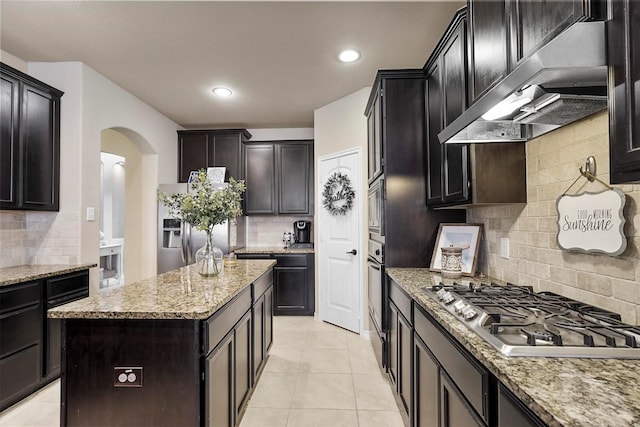 kitchen with light stone counters, appliances with stainless steel finishes, arched walkways, and under cabinet range hood