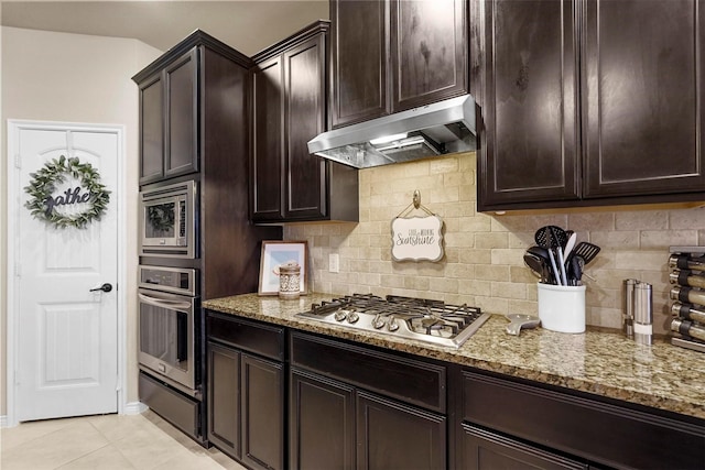 kitchen featuring a warming drawer, under cabinet range hood, light stone counters, tasteful backsplash, and appliances with stainless steel finishes