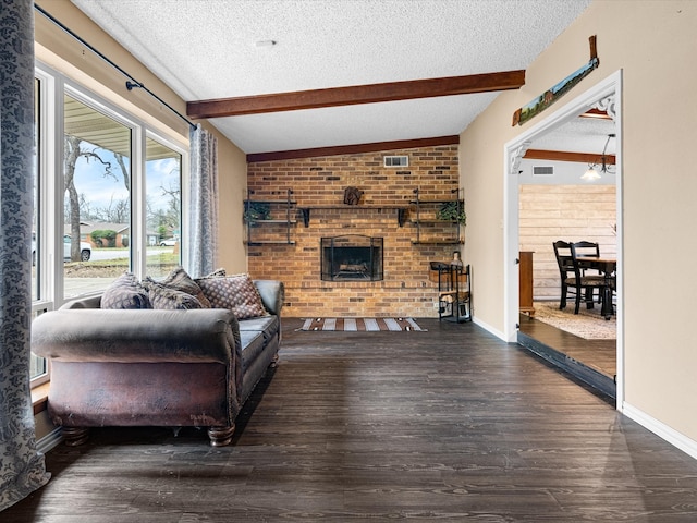 living room featuring beam ceiling, a textured ceiling, wood finished floors, baseboards, and a brick fireplace