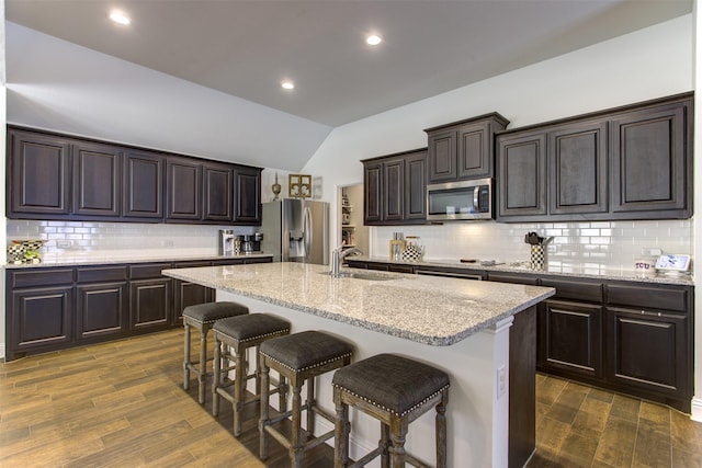 kitchen featuring a sink, dark wood finished floors, stainless steel appliances, a breakfast bar area, and vaulted ceiling