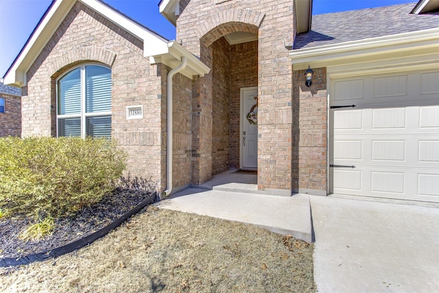 entrance to property with a garage, brick siding, and roof with shingles