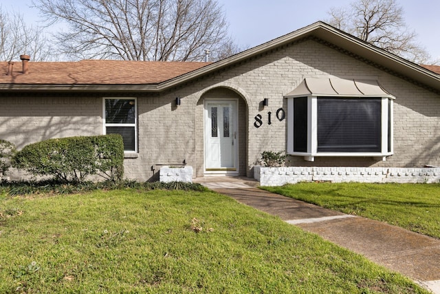 view of front of home featuring a front lawn, brick siding, and a shingled roof