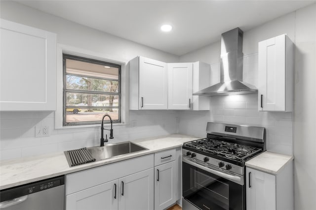 kitchen featuring a sink, backsplash, white cabinetry, stainless steel appliances, and wall chimney exhaust hood