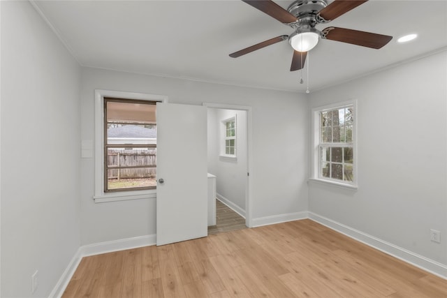 empty room featuring light wood-style flooring, plenty of natural light, a ceiling fan, and baseboards