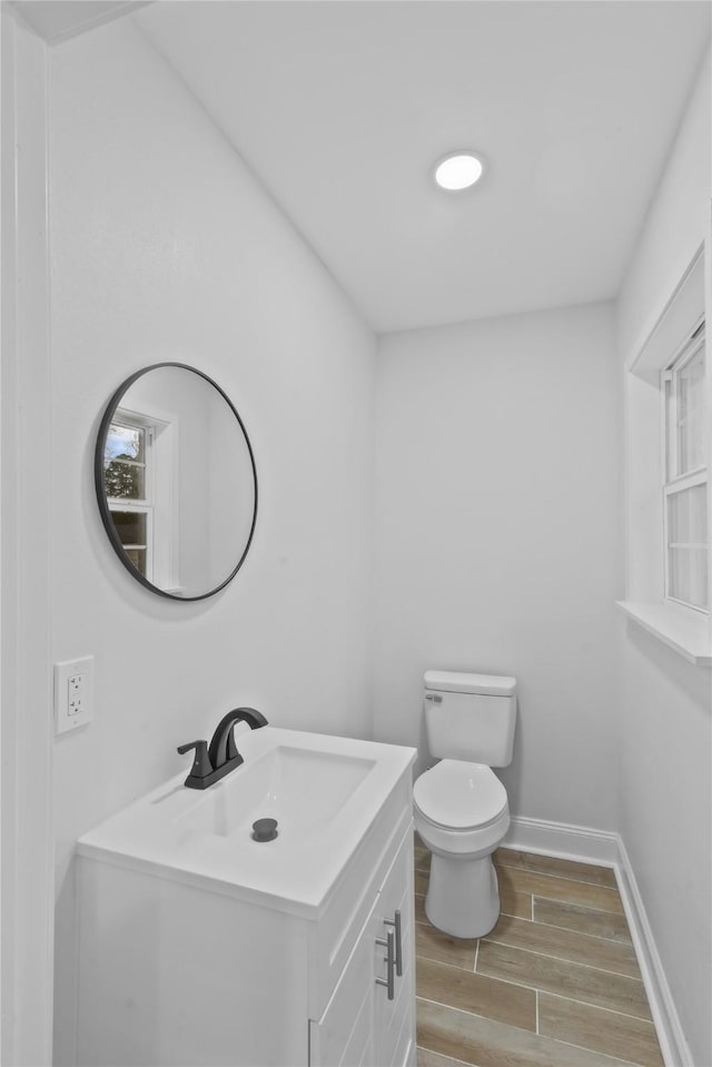 half bathroom featuring vanity, toilet, baseboards, and wood tiled floor