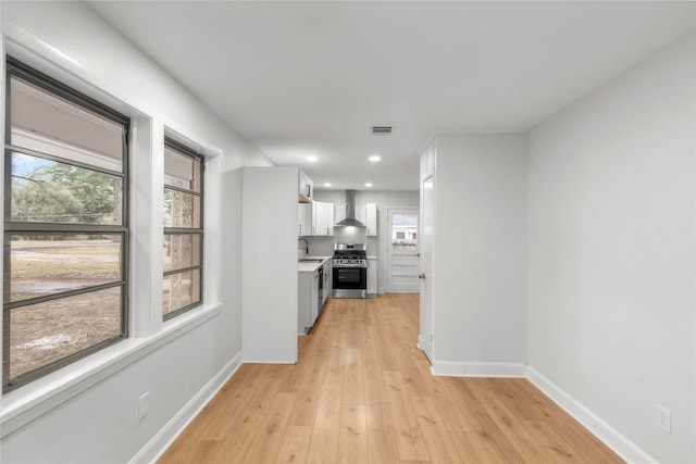 kitchen featuring a wealth of natural light, visible vents, white cabinets, wall chimney range hood, and stainless steel range with gas stovetop