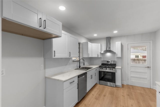 kitchen featuring tasteful backsplash, appliances with stainless steel finishes, white cabinets, wall chimney exhaust hood, and a sink