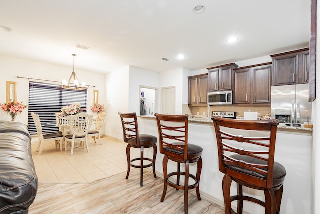 kitchen with visible vents, backsplash, dark brown cabinets, a breakfast bar, and stainless steel appliances