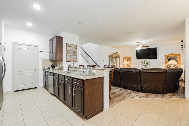 kitchen with dark brown cabinetry, appliances with stainless steel finishes, a peninsula, light tile patterned flooring, and a sink