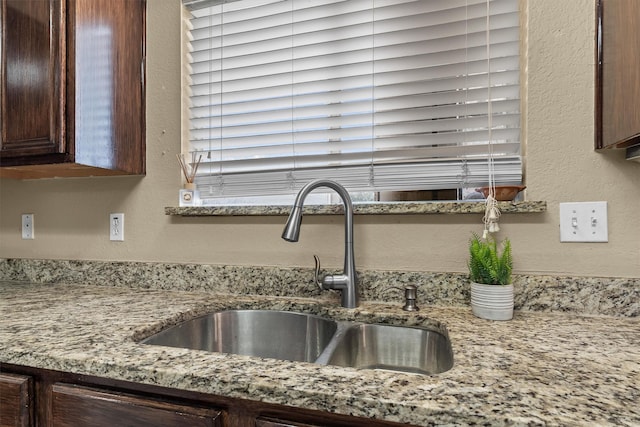 kitchen with a sink, light stone countertops, dark brown cabinetry, and a textured wall