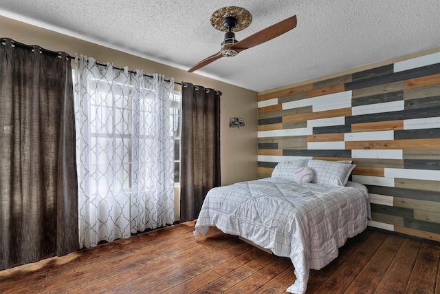 bedroom featuring wooden walls, a textured ceiling, a ceiling fan, and wood-type flooring