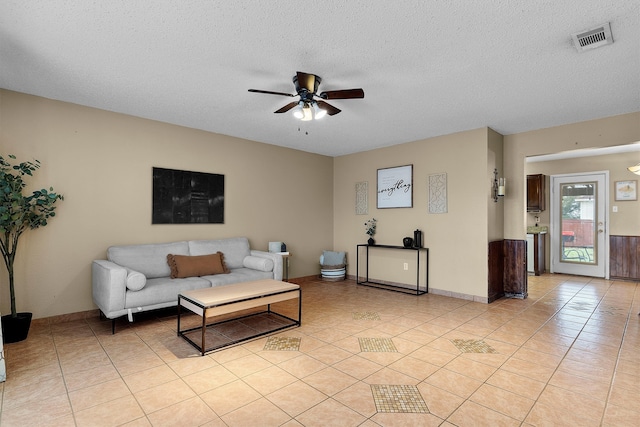 living area featuring light tile patterned floors, visible vents, a textured ceiling, and a ceiling fan