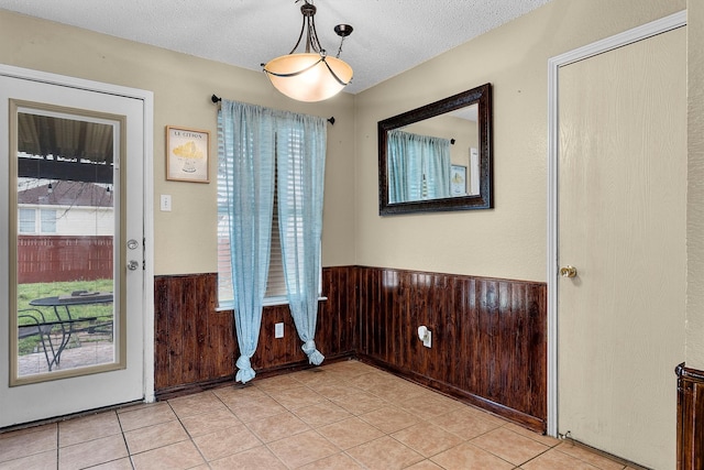 entrance foyer with light tile patterned floors, a wainscoted wall, wooden walls, and a textured ceiling