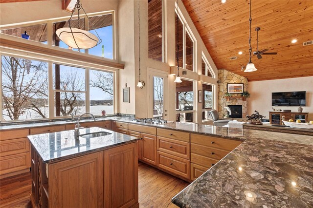 kitchen featuring a sink, dark stone countertops, wood finished floors, a stone fireplace, and wooden ceiling