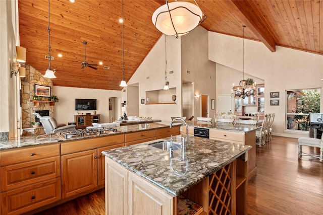 kitchen with a center island with sink, dark stone countertops, open floor plan, dark wood finished floors, and stainless steel gas cooktop