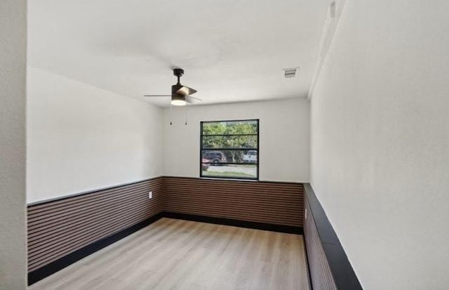 spare room featuring visible vents, wainscoting, a ceiling fan, and wood finished floors