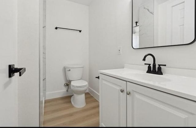 bathroom featuring baseboards, toilet, wood finished floors, and vanity