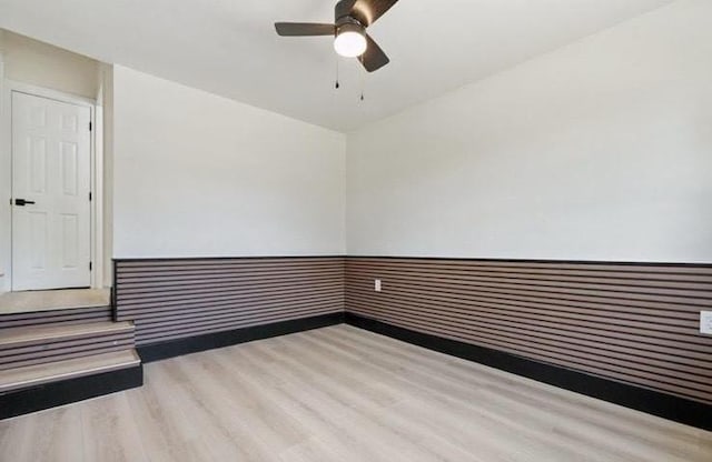 empty room with wainscoting, ceiling fan, and wood finished floors