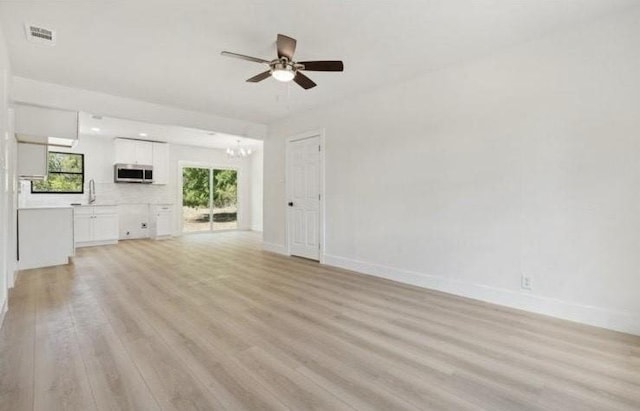 unfurnished living room featuring visible vents, baseboards, light wood-style flooring, ceiling fan with notable chandelier, and a sink