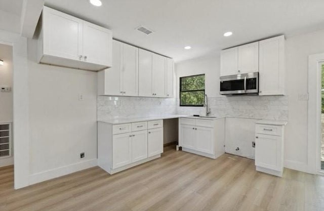 kitchen with light wood finished floors, stainless steel microwave, tasteful backsplash, white cabinetry, and a sink