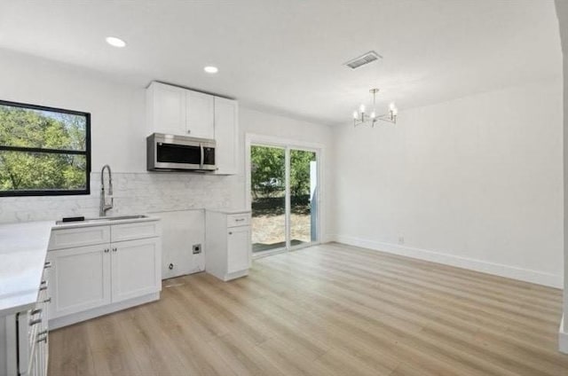 kitchen with a sink, stainless steel microwave, white cabinetry, light wood finished floors, and decorative backsplash