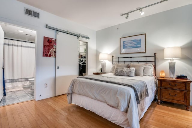 bedroom with visible vents, light wood-style flooring, a walk in closet, and a barn door