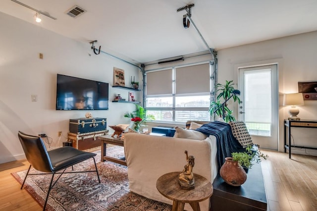 living area with rail lighting, a garage, wood finished floors, and visible vents