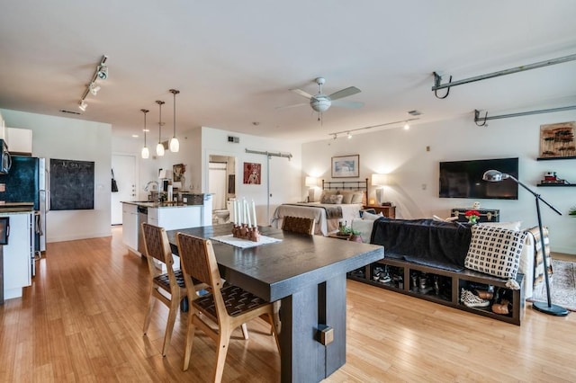 dining space with light wood-type flooring, visible vents, track lighting, a ceiling fan, and a barn door