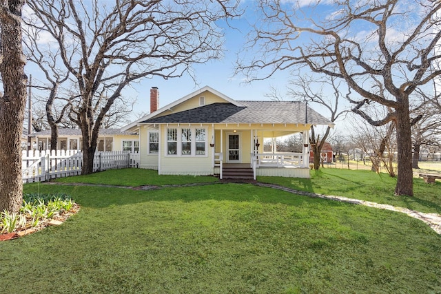 view of front facade with a shingled roof, a front lawn, fence, and a chimney