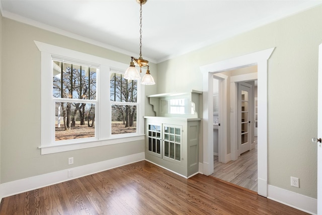 unfurnished dining area featuring baseboards, wood finished floors, and ornamental molding