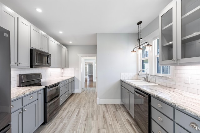 kitchen with a sink, light stone counters, gray cabinetry, and stainless steel appliances