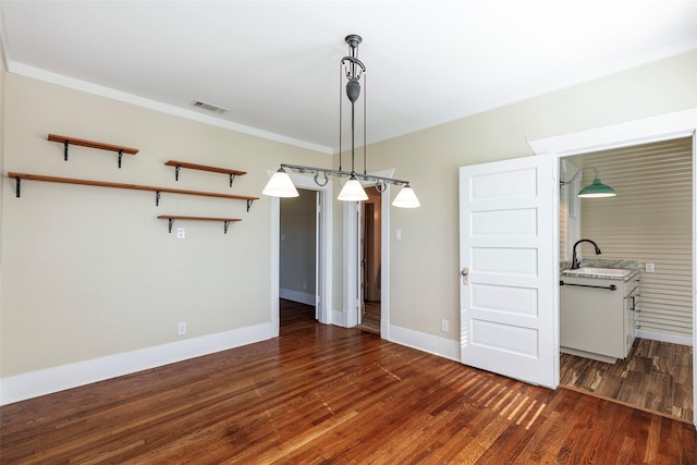 unfurnished dining area with visible vents, a sink, wood finished floors, crown molding, and baseboards