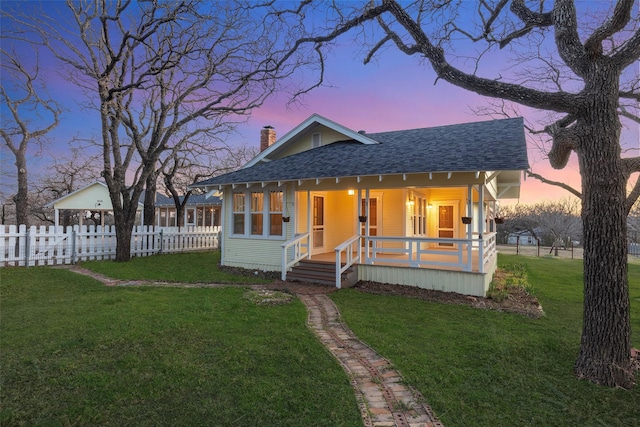 view of front of home with a front lawn, a porch, fence, roof with shingles, and a chimney