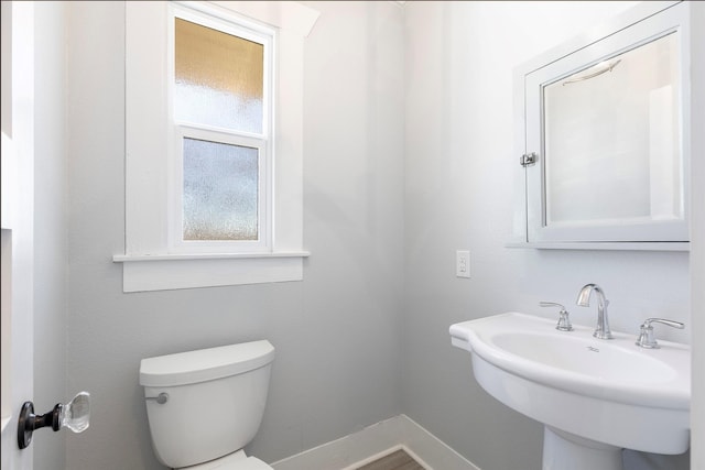 half bathroom featuring toilet, baseboards, and a sink