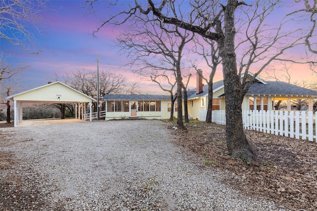 ranch-style house with a carport, a sunroom, gravel driveway, and fence