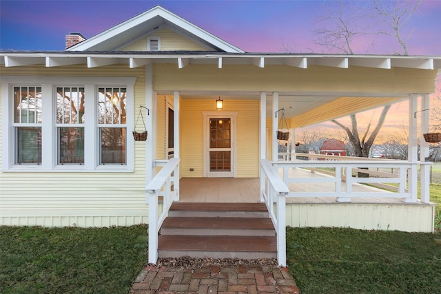 exterior entry at dusk featuring a porch and a chimney