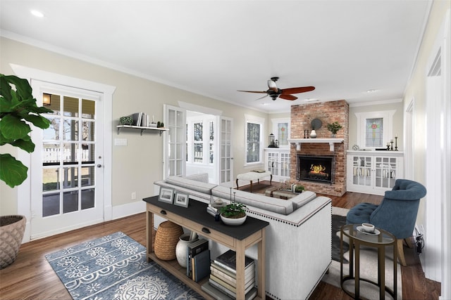 living room featuring a ceiling fan, wood finished floors, a fireplace, crown molding, and baseboards