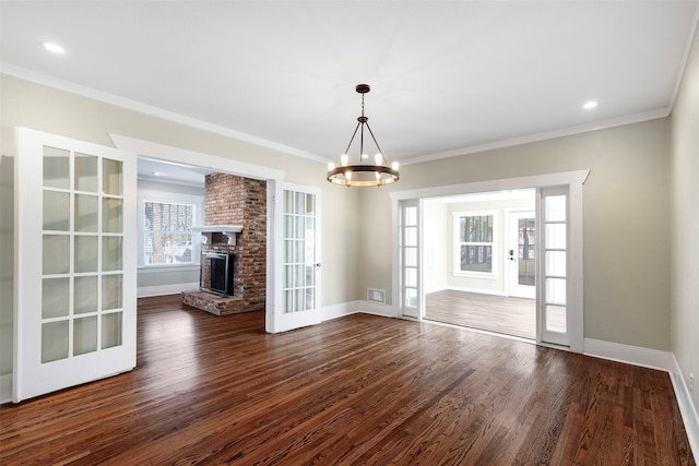 unfurnished dining area with a notable chandelier, a fireplace, crown molding, baseboards, and dark wood-style flooring