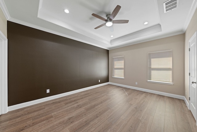 empty room featuring visible vents, crown molding, baseboards, light wood-type flooring, and a tray ceiling