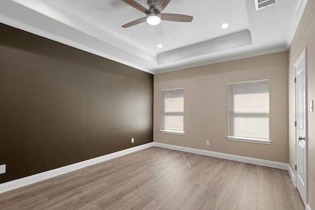 empty room with a raised ceiling, light wood-style flooring, baseboards, and ornamental molding