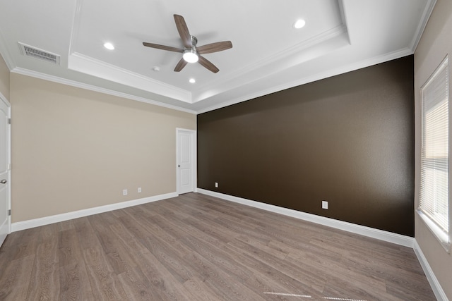 empty room featuring visible vents, ornamental molding, wood finished floors, baseboards, and a raised ceiling