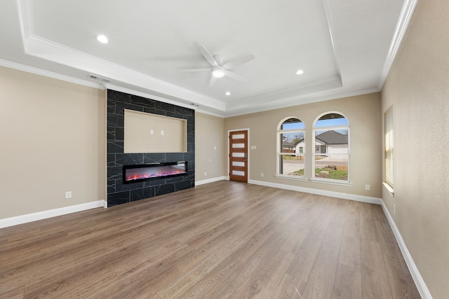 unfurnished living room with wood finished floors, baseboards, a premium fireplace, a tray ceiling, and crown molding