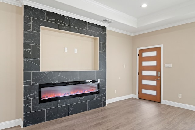 foyer entrance with wood finished floors, a tray ceiling, recessed lighting, a fireplace, and ornamental molding