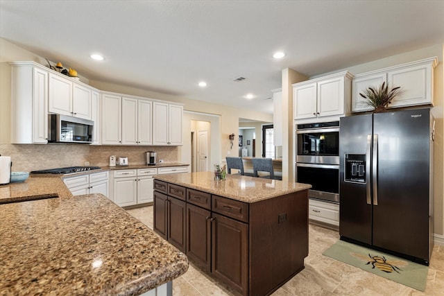 kitchen featuring backsplash, a kitchen island, light stone countertops, appliances with stainless steel finishes, and white cabinetry