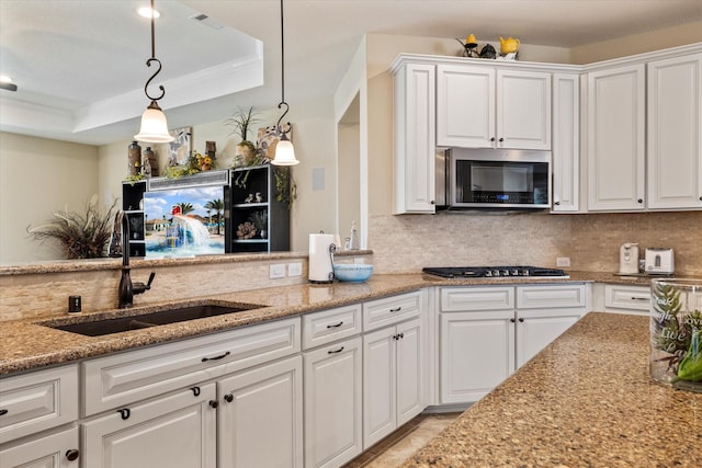 kitchen featuring a sink, a tray ceiling, backsplash, stainless steel appliances, and white cabinets