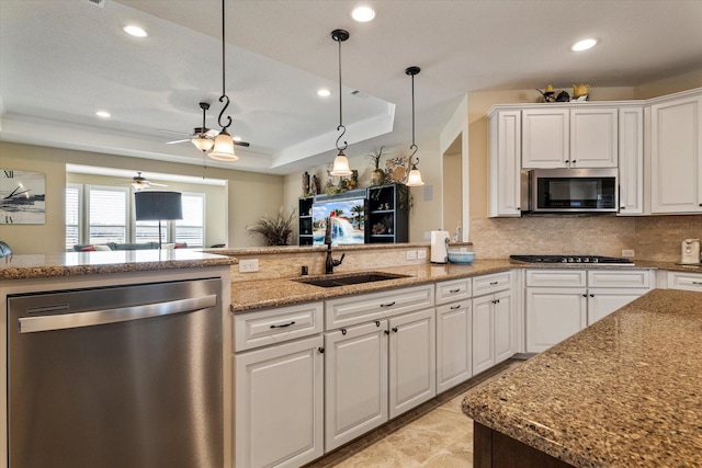 kitchen with tasteful backsplash, appliances with stainless steel finishes, white cabinetry, a raised ceiling, and a sink