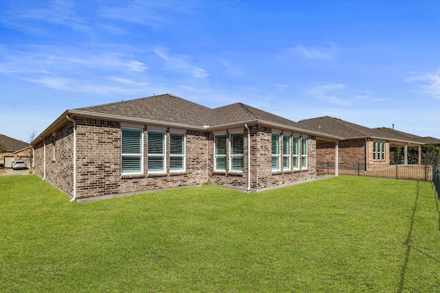 back of property with a lawn, a shingled roof, brick siding, and fence